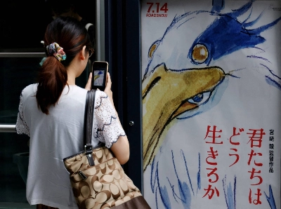 A woman takes a picture of the poster for the new Hayao Miyazaki film, “The Boy and the Heron.” A woman takes a picture of the poster for the new Hayao Miyazaki film, “The Boy and the Heron.”