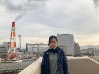Erina Imai, a plaintiff in a climate lawsuit, poses in front of the coal-fired Kobe Power Plant in Kobe. The red and white tower behind her is private power generation equipment operated by Kobe Steel and is releasing water vapor, not smoke. | COURTESY OF ERINA IMAI