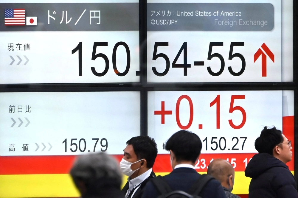 People pass an electronic board showing the rate of the yen against the dollar on a street in Tokyo on Wednesday. People pass an electronic board showing the rate of the yen against the dollar on a street in Tokyo on Wednesday.