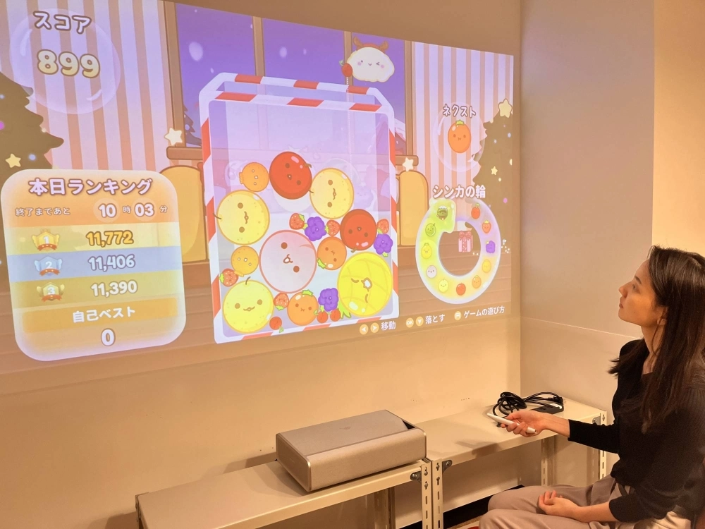 An Aladdin X staff member plays Suika Game on its home projector in Tokyo on Friday. Suika Game was originally developed for the company's line of home projectors. An Aladdin X staff member plays Suika Game on its home projector in Tokyo on Friday. Suika Game was originally developed for the company's line of home projectors.
