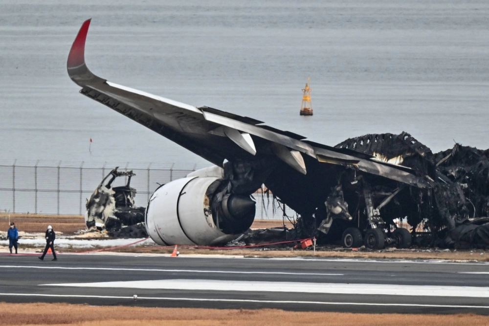Officials examine the burned wreckage of a Japan Airlines passenger plane on the tarmac at Haneda Airport in Tokyo on Wednesday. Officials examine the burned wreckage of a Japan Airlines passenger plane on the tarmac at Haneda Airport in Tokyo on Wednesday.
