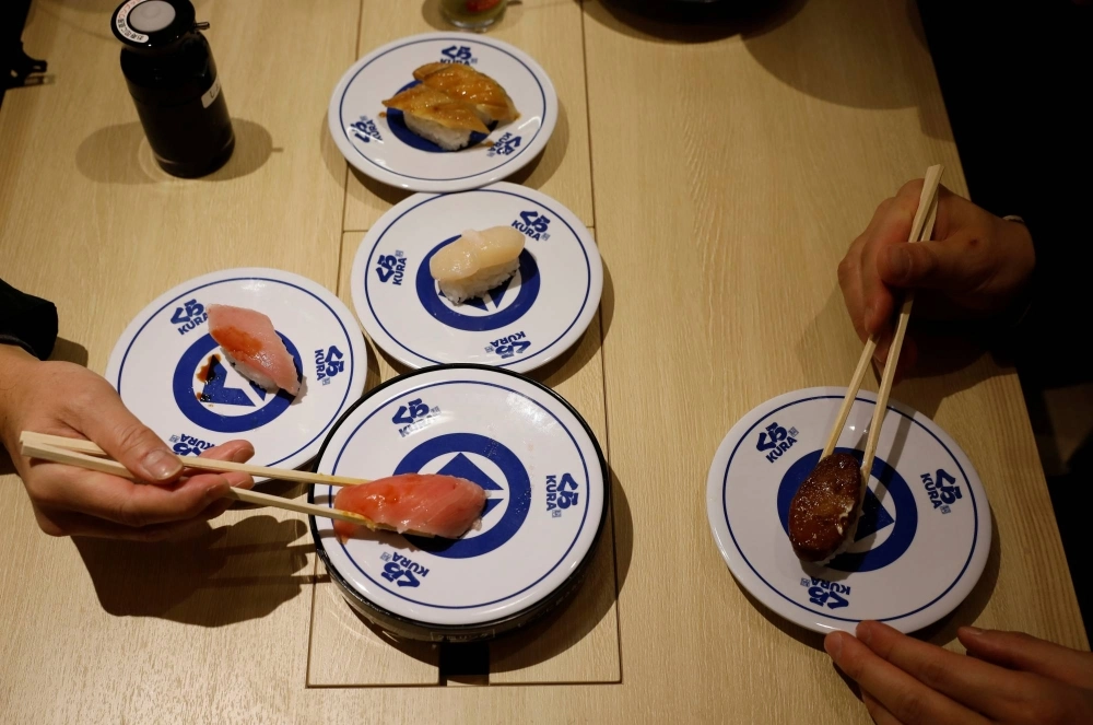 As Kura has grown, so has the hype, with diners sometimes enduring seven-hour waits to try its automated sushi-serving machines and dishes under plastic domes brought to the table on a revolving belt.  As Kura has grown, so has the hype, with diners sometimes enduring seven-hour waits to try its automated sushi-serving machines and dishes under plastic domes brought to the table on a revolving belt.