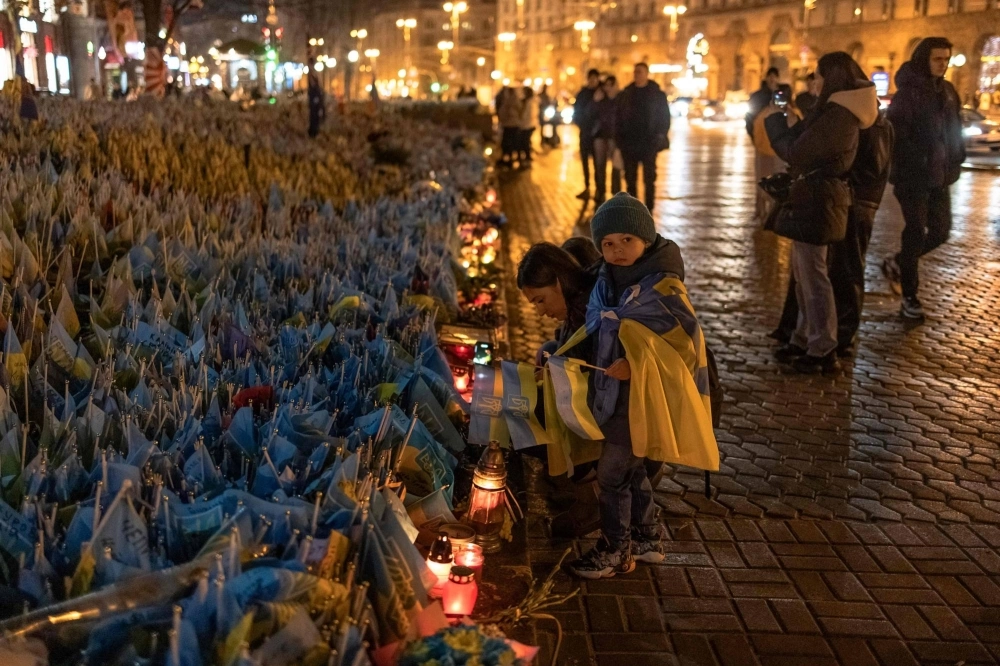 A woman and children place flags for friends who are in the Ukrainian military at Independence Square in Kyiv on Saturday.  A woman and children place flags for friends who are in the Ukrainian military at Independence Square in Kyiv on Saturday.
