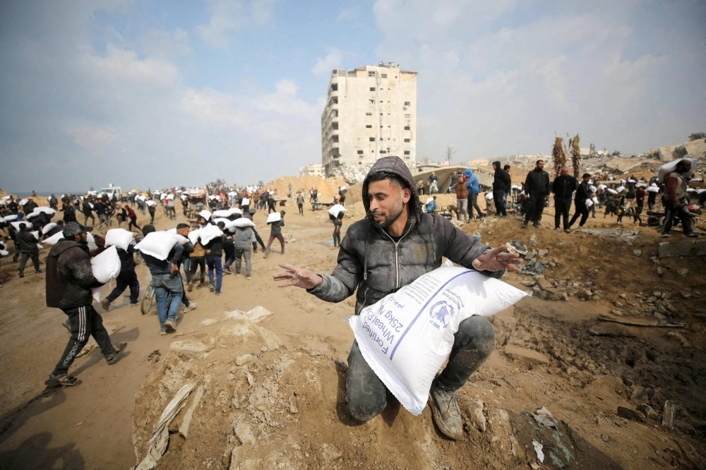 Palestinians carry bags of flour they grabbed from an aid truck in mid February near an Israeli checkpoint as Gaza residents face crisis levels of hunger amid the ongoing conflict between Israel and Hamas.  Palestinians carry bags of flour they grabbed from an aid truck in mid February near an Israeli checkpoint as Gaza residents face crisis levels of hunger amid the ongoing conflict between Israel and Hamas.