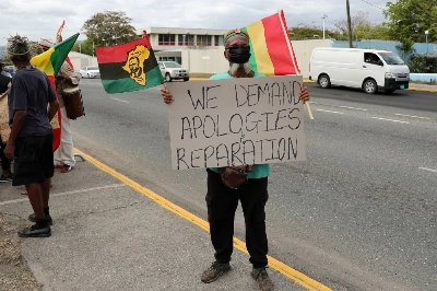 A protester demands the United Kingdom make reparations for slavery, outside the British High Commission, in Kingston, Jamaica, in March 2022.  A protester demands the United Kingdom make reparations for slavery, outside the British High Commission, in Kingston, Jamaica, in March 2022.