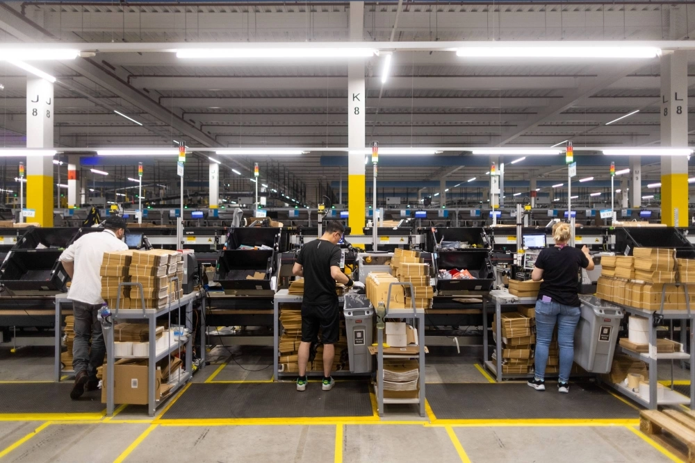 Employees place items into boxes and envelopes at an Amazon fulfillment center. Employees place items into boxes and envelopes at an Amazon fulfillment center.