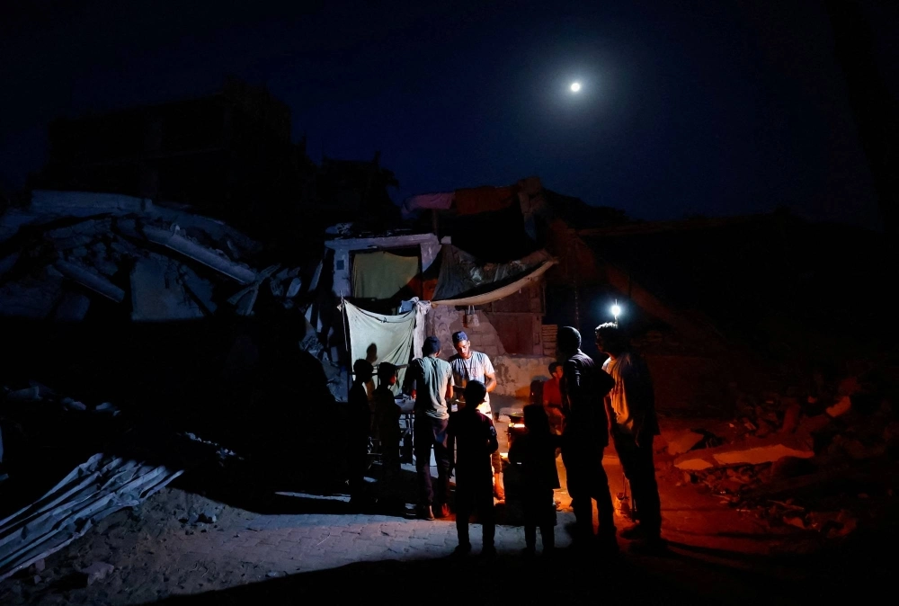 Palestinians gather amid power cut near houses destroyed during Israel's military offensive in Khan Younis, in the southern Gaza Strip, on Wednesday.  Palestinians gather amid power cut near houses destroyed during Israel's military offensive in Khan Younis, in the southern Gaza Strip, on Wednesday.