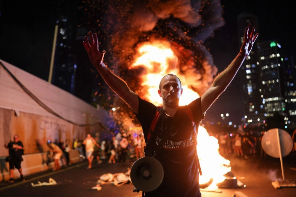 A man raises his arms in front of burning wooden pallets on Sunday as protesters block Tel Aviv's Ayalon highway during an antigovernment rally calling for the release of Israelis held hostage by Palestinian militants in Gaza since October. A man raises his arms in front of burning wooden pallets on Sunday as protesters block Tel Aviv's Ayalon highway during an antigovernment rally calling for the release of Israelis held hostage by Palestinian militants in Gaza since October.