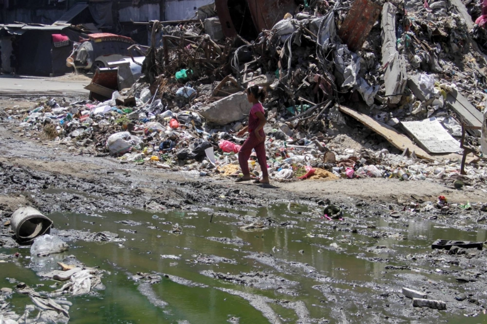 A Palestinian girl walks near a puddle of wastewater and piles of garbage and debris amid the spread of skin infections in the northern Gaza Strip on Aug. 5. A Palestinian girl walks near a puddle of wastewater and piles of garbage and debris amid the spread of skin infections in the northern Gaza Strip on Aug. 5.