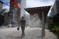 A pedestrian walks next to a cooling mist spray in the Ginza district of Tokyo on July 19. | Bloomberg