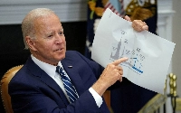 U.S. President Joe Biden holds up a wind turbine size comparison chart while attending a meeting with governors, labor leaders, and private companies launching the Federal-State Offshore Wind Implementation Partnership, at the White House in Washington in 2022. | REUTERS