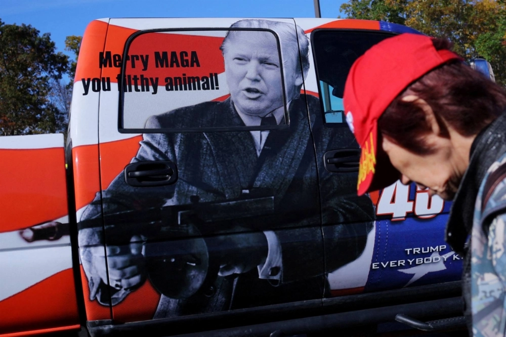 An attendee walks past a picture of Republican presidential nominee and former U.S. President Donald Trump holding a gun and the words "Merry MAGA you filthy animal!" at the Rod of Iron Freedom Festival, which the organizers call "the largest open carry rally in America," in Greeley, Pennsylvania, on Oct. 12. An attendee walks past a picture of Republican presidential nominee and former U.S. President Donald Trump holding a gun and the words "Merry MAGA you filthy animal!" at the Rod of Iron Freedom Festival, which the organizers call "the largest open carry rally in America," in Greeley, Pennsylvania, on Oct. 12.