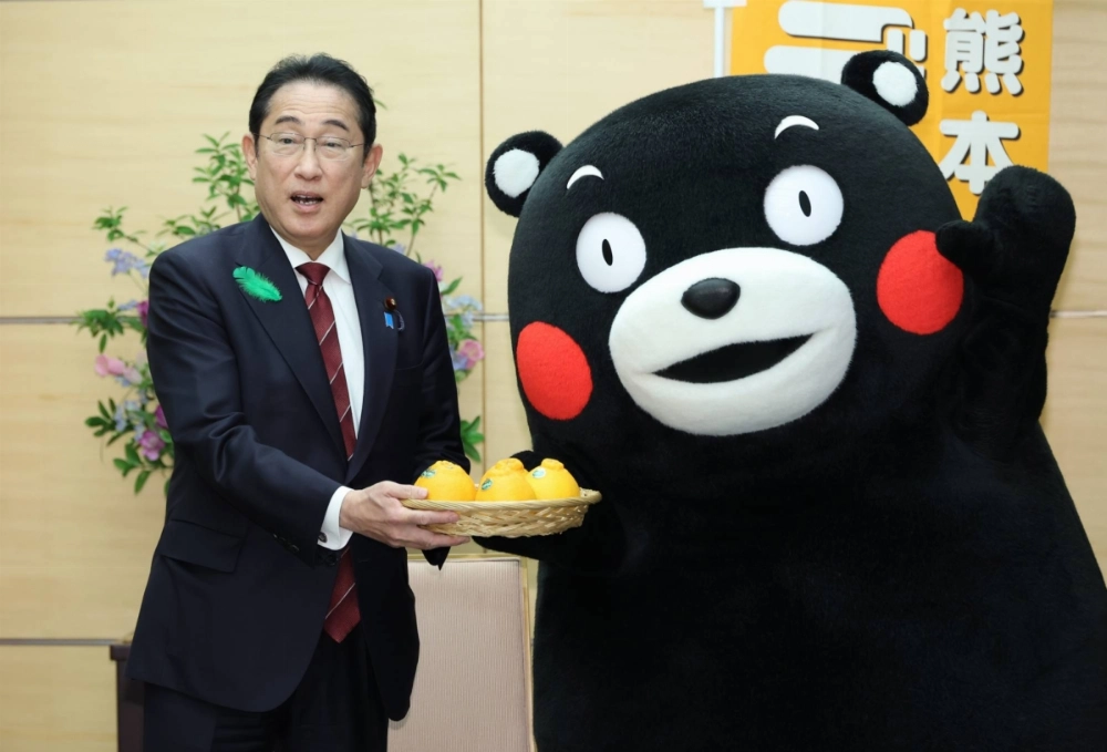 Former Prime Minister Fumio Kishida accepts a gift of 'dekopon' citruses, a specialty product and symbol of Kumamoto Prefecture, from Kumamon, itself a mascot and instantly recognizeable symbol of the region. Former Prime Minister Fumio Kishida accepts a gift of 'dekopon' citruses, a specialty product and symbol of Kumamoto Prefecture, from Kumamon, itself a mascot and instantly recognizeable symbol of the region.