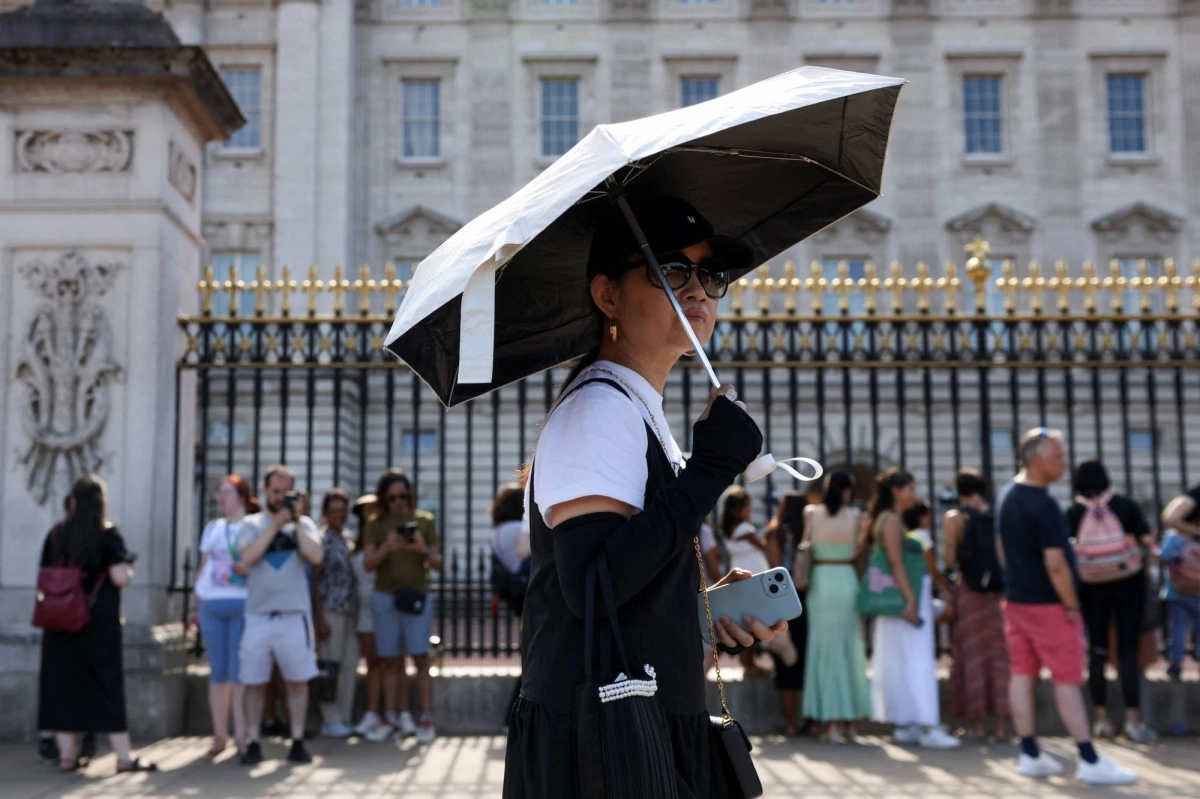 A woman shelters from the summer sun under an umbrella at Buckingham Palace in London. A woman shelters from the summer sun under an umbrella at Buckingham Palace in London.