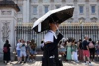 A woman shelters from the summer sun under an umbrella at Buckingham Palace in London. | REUTERS