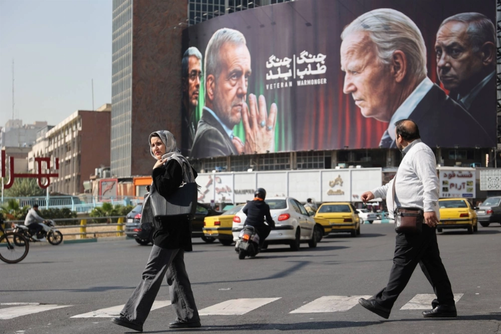 Iranians walk next to an anti-U.S. and Israeli billboard with pictures on the left of Iranian President Masoud Pezeshkian and Iranian Armed Forces Chief of Staff, Maj. Gen. Mohammad Bagheri, and on the right, U.S. President Joe Biden and Israel's Prime Minister Benjamin Netanyahu, on a street in Tehran on Sunday. Iranians walk next to an anti-U.S. and Israeli billboard with pictures on the left of Iranian President Masoud Pezeshkian and Iranian Armed Forces Chief of Staff, Maj. Gen. Mohammad Bagheri, and on the right, U.S. President Joe Biden and Israel's Prime Minister Benjamin Netanyahu, on a street in Tehran on Sunday.