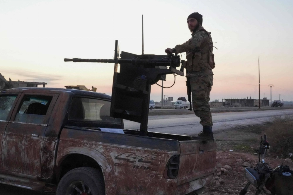 An anti-regime fighter operates a truck-mounted gun as displaced Syrian Kurds drive vehicles loaded with their belongings along the Aleppo-Raqqa highway. An anti-regime fighter operates a truck-mounted gun as displaced Syrian Kurds drive vehicles loaded with their belongings along the Aleppo-Raqqa highway.