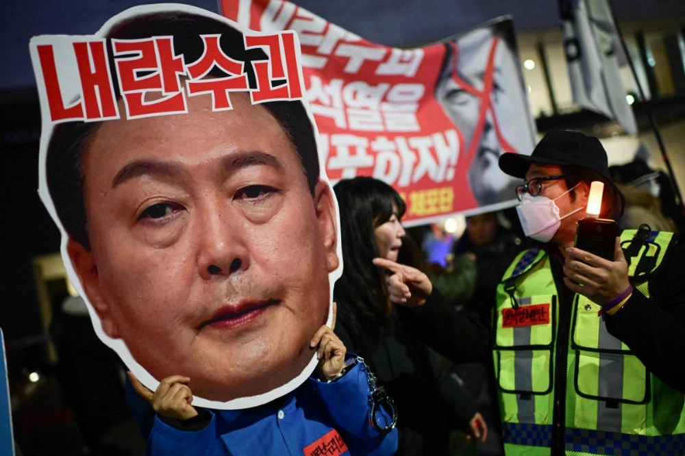 A protester holding a cardboard reading "Leader of insurgents" on an image depicting the face of South Korea's President Yoon Suk Yeol takes part in a protest calling for his ouster outside the National Assembly in Seoul on Sunday. A protester holding a cardboard reading "Leader of insurgents" on an image depicting the face of South Korea's President Yoon Suk Yeol takes part in a protest calling for his ouster outside the National Assembly in Seoul on Sunday.