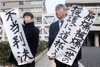The plaintiffs' lawyers hold paper with phrases such as "unjust verdict," after the appeal court ruling in the second-generation hibakusha lawsuit, in Hiroshima Prefecture on Friday. | Jiji