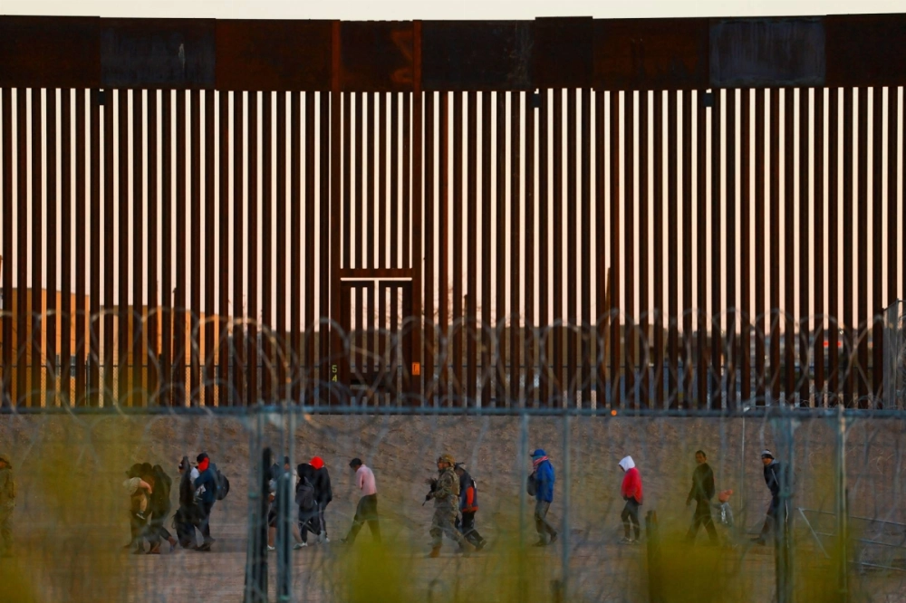 Migrants seeking asylum gather near the border wall between the United States and Mexico after crossing a razor wire fence deployed to inhibit their crossing, as a member of the Texas National Guard escorts them on Dec. 19. Migrants seeking asylum gather near the border wall between the United States and Mexico after crossing a razor wire fence deployed to inhibit their crossing, as a member of the Texas National Guard escorts them on Dec. 19.