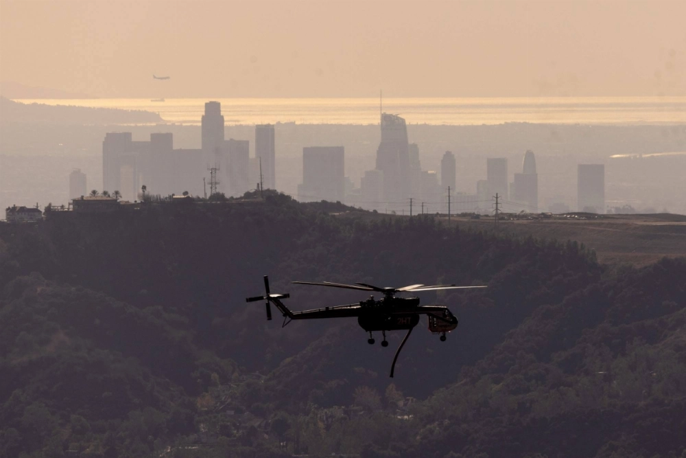 A firefighting helicopter flies past downtown Los Angeles as it goes back and forth dropping water on the Eaton Fire near Altadina, California, on Monday. At least two rounds of vicious, dry Santa Ana winds are expected to blast through Southern California early this week, bringing powerful gusts that will challenge fire crews struggling to contain two destructive blazes and likely force thousands more residents to evacuate.  A firefighting helicopter flies past downtown Los Angeles as it goes back and forth dropping water on the Eaton Fire near Altadina, California, on Monday. At least two rounds of vicious, dry Santa Ana winds are expected to blast through Southern California early this week, bringing powerful gusts that will challenge fire crews struggling to contain two destructive blazes and likely force thousands more residents to evacuate.