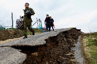 A Self-Defense Forces member leads residents in Fukamimachi, a village in Wajima, Ishikawa Prefecture, to a rescue helicopter, on a destroyed road in January last year. | Reuters