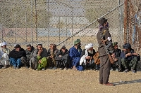 A Taliban security personnel stands guard as Afghan men wait to receive winter aid packages in Kandahar in January. | AFP-JIJI