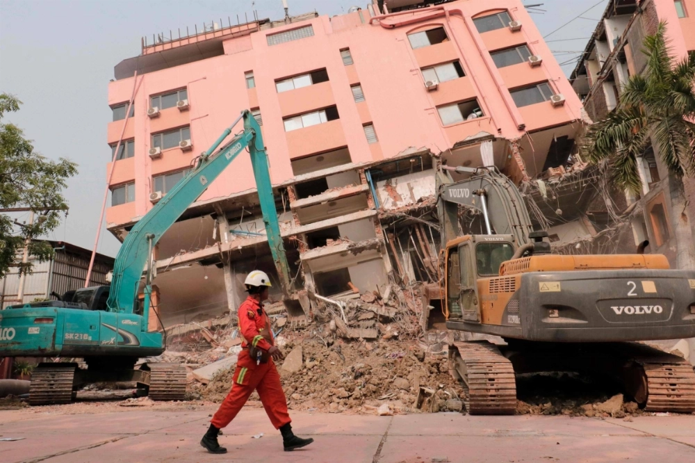 A rescue worker walks past construction equipment being used to clear rubble at the site of a collapsed building in Mandalay, Myanmar, on Saturday. A rescue worker walks past construction equipment being used to clear rubble at the site of a collapsed building in Mandalay, Myanmar, on Saturday.