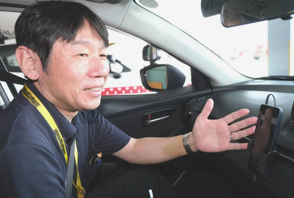 Shingo Kato, assistant manager at Homechigiru Driving School in Ise, Mie Prefecture, rides in a training vehicle with a smartphone equipped with the school’s translation app. Shingo Kato, assistant manager at Homechigiru Driving School in Ise, Mie Prefecture, rides in a training vehicle with a smartphone equipped with the school’s translation app.
