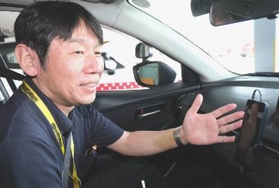 Shingo Kato, assistant manager at Homechigiru Driving School in Ise, Mie Prefecture, rides in a training vehicle with a smartphone equipped with the school’s translation app. Shingo Kato, assistant manager at Homechigiru Driving School in Ise, Mie Prefecture, rides in a training vehicle with a smartphone equipped with the school’s translation app.