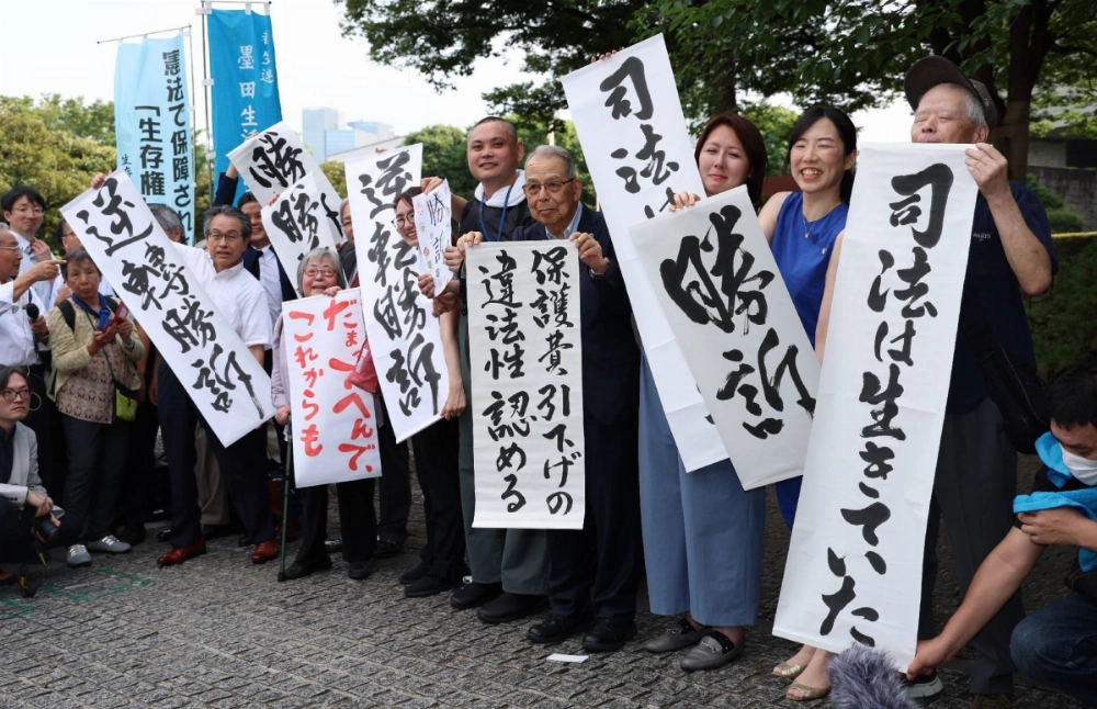 Plaintiffs of lawsuits on welfare benefit reductions hold up signs celebrating their victory in Tokyo on Friday following the Supreme Court's ruling in favor of them. Plaintiffs of lawsuits on welfare benefit reductions hold up signs celebrating their victory in Tokyo on Friday following the Supreme Court's ruling in favor of them.