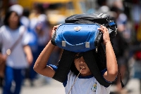 A student uses her bag as protection against the sun outside an elementary school in Manila in April 2024. | REUTERS