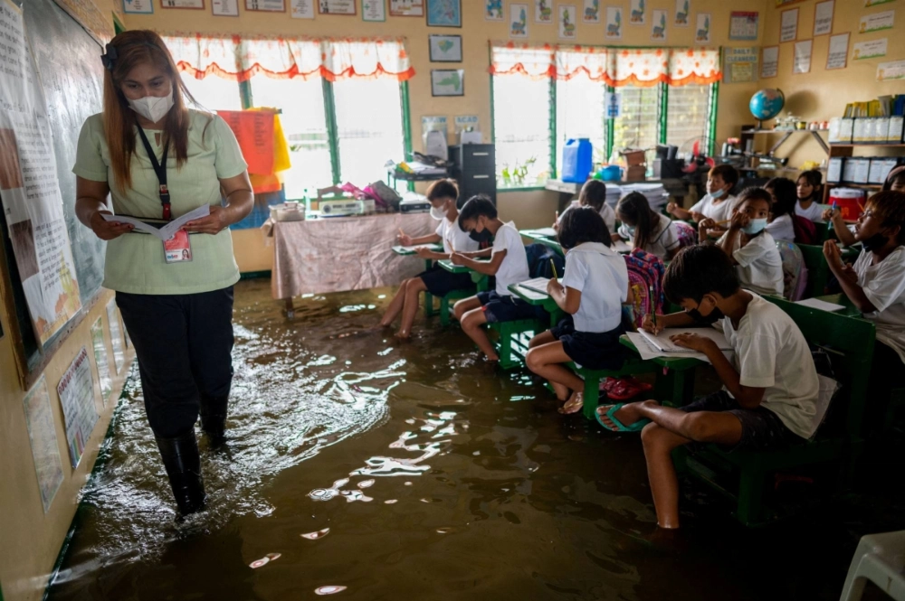 A public school teacher leads the class during the first day of in-person classes, at a school flooded due to high tide, in Macabebe, Pampanga province, Philippines, in August 2022. A public school teacher leads the class during the first day of in-person classes, at a school flooded due to high tide, in Macabebe, Pampanga province, Philippines, in August 2022.