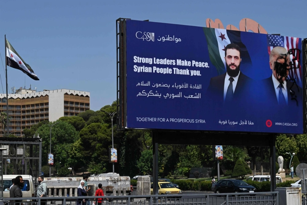 A picture shows a promotional poster bearing the portrait of Syria's interim president, Ahmad al-Sharaa, next to a defaced portrait of U.S. President Donald Trump in Damascus on Wednesday. A picture shows a promotional poster bearing the portrait of Syria's interim president, Ahmad al-Sharaa, next to a defaced portrait of U.S. President Donald Trump in Damascus on Wednesday.