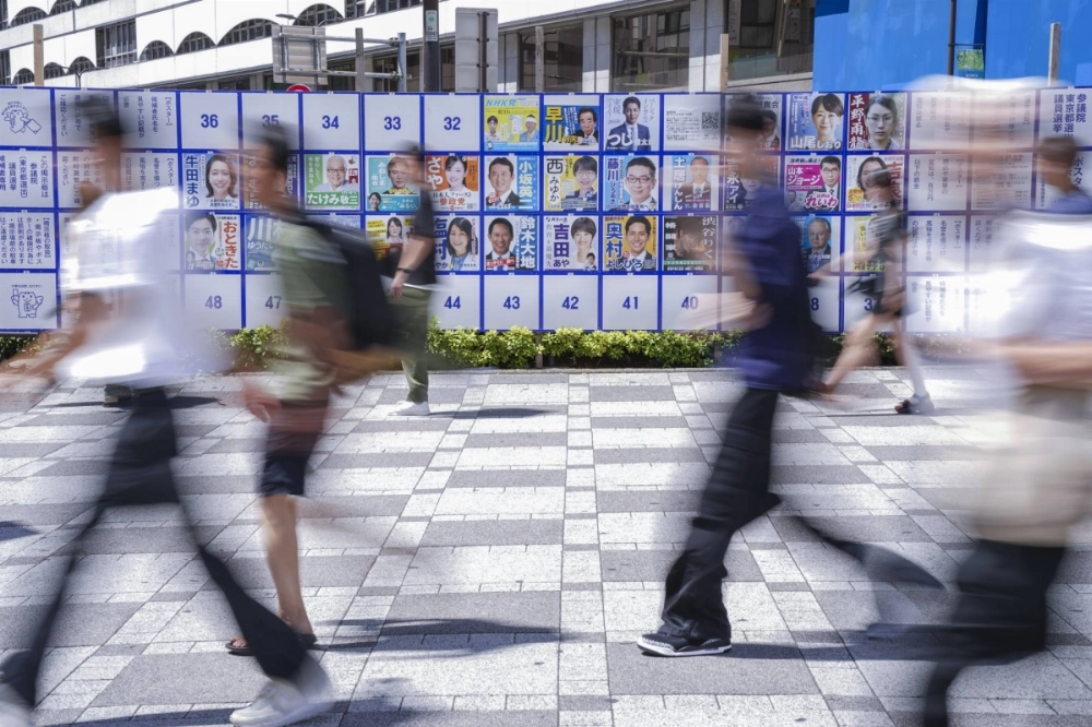 Pedestrians walk in front of an election notice board displaying posters of candidates in Tokyo on Sunday. Pedestrians walk in front of an election notice board displaying posters of candidates in Tokyo on Sunday.