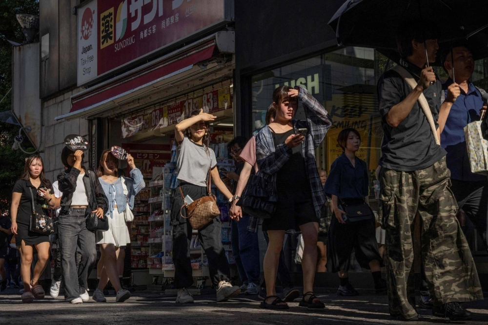 People shield their eyes from the sun as they walk through a street on a hot day in Tokyo on July 26.  People shield their eyes from the sun as they walk through a street on a hot day in Tokyo on July 26.