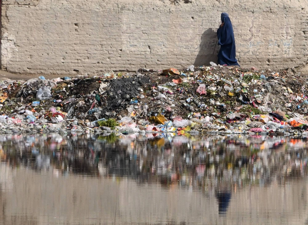 An Afghan woman walks next to a pile of trash full of plastic bags in Kabul.  An Afghan woman walks next to a pile of trash full of plastic bags in Kabul.