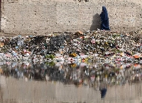 An Afghan woman walks next to a pile of trash full of plastic bags in Kabul.  | AFP-Jiji