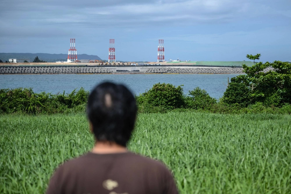 Takemasa Kinjo, who was a high school student when his mother was killed by a U.S. Marine in 1974, looks on at the construction site of the new Henoko military base for U.S. forces near his residence in Nago, Okinawa Prefecture, in June.  Takemasa Kinjo, who was a high school student when his mother was killed by a U.S. Marine in 1974, looks on at the construction site of the new Henoko military base for U.S. forces near his residence in Nago, Okinawa Prefecture, in June.