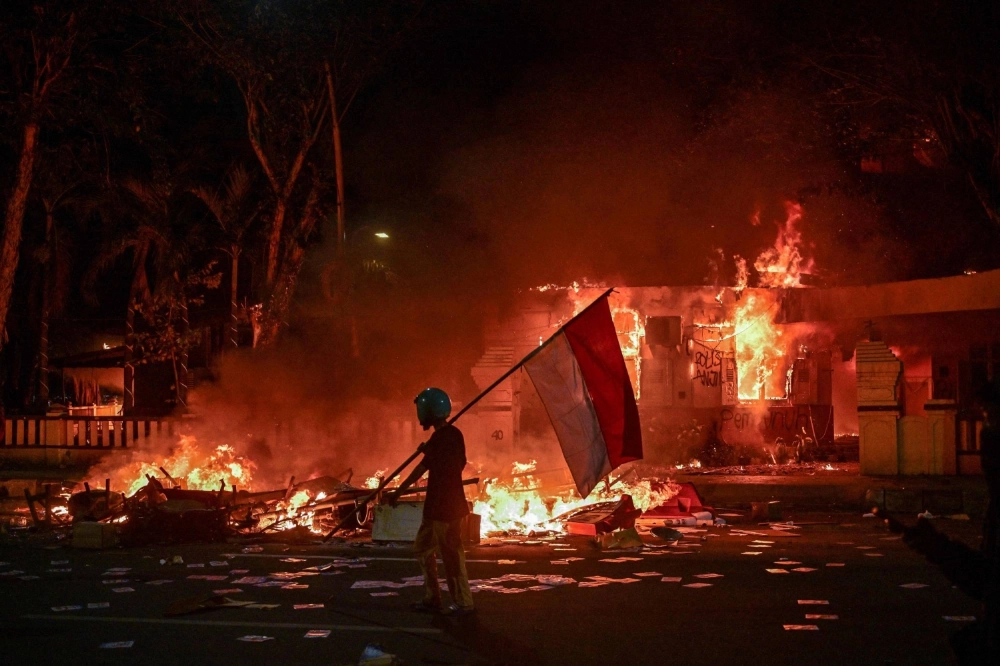 A protester carries an Indonesian flag past a police headquarters that was set on fire and looted during demonstrations in Surabaya, Indonesia, on Sunday. A protester carries an Indonesian flag past a police headquarters that was set on fire and looted during demonstrations in Surabaya, Indonesia, on Sunday.