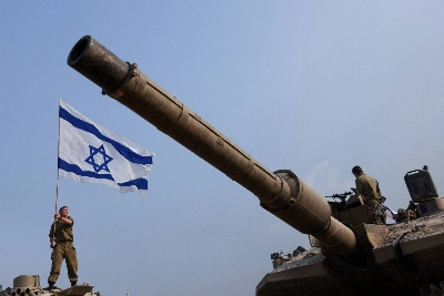 A soldier on a tank waves an Israeli flag amid the ongoing conflict between Israel and the Palestinian Islamist group Hamas near the Israel-Gaza border in January 2024.  A soldier on a tank waves an Israeli flag amid the ongoing conflict between Israel and the Palestinian Islamist group Hamas near the Israel-Gaza border in January 2024.
