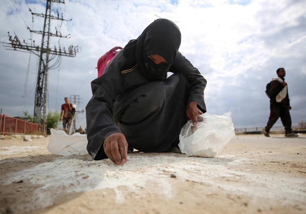 A woman collects flour from the ground as Palestinians receive aid supplies from the U.S.-backed Gaza Humanitarian Foundation in the central Gaza Strip in August. A woman collects flour from the ground as Palestinians receive aid supplies from the U.S.-backed Gaza Humanitarian Foundation in the central Gaza Strip in August.