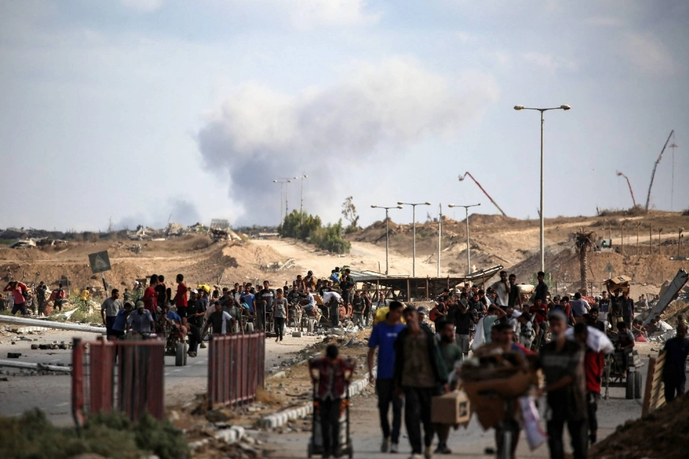 A plume of smoke rises in the background as Palestinians return from a food distribution point run by the U.S. and Israeli-backed Gaza Humanitarian Foundation group, near the Netsarim corridor in the central Gaza Strip on Sunday. A plume of smoke rises in the background as Palestinians return from a food distribution point run by the U.S. and Israeli-backed Gaza Humanitarian Foundation group, near the Netsarim corridor in the central Gaza Strip on Sunday.