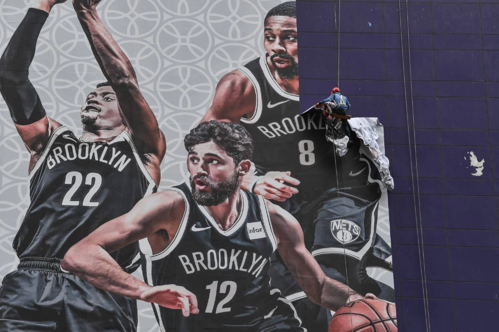 A worker removes a promotional banner from a building for an NBA preseason game in Shanghai in October 2019. The NBA returns to the lucrative Chinese market this week after a six-year absence.  A worker removes a promotional banner from a building for an NBA preseason game in Shanghai in October 2019. The NBA returns to the lucrative Chinese market this week after a six-year absence.