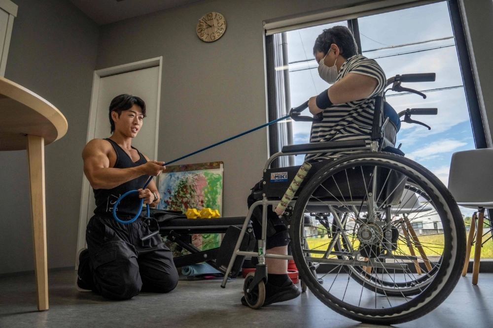 Care worker and bodybuilder Hokuto Tatsumi helps a woman train at a care home for people with disabilities operated by Visionary in Aichi prefecture.  Care worker and bodybuilder Hokuto Tatsumi helps a woman train at a care home for people with disabilities operated by Visionary in Aichi prefecture.