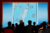 2022年10月,在北京舉辦的一場展覽上,參觀者站在一塊巨型螢幕前,螢幕上顯示中國於2022年8月在台灣週邊地區舉行軍事演習的地點地圖。 (路透社)