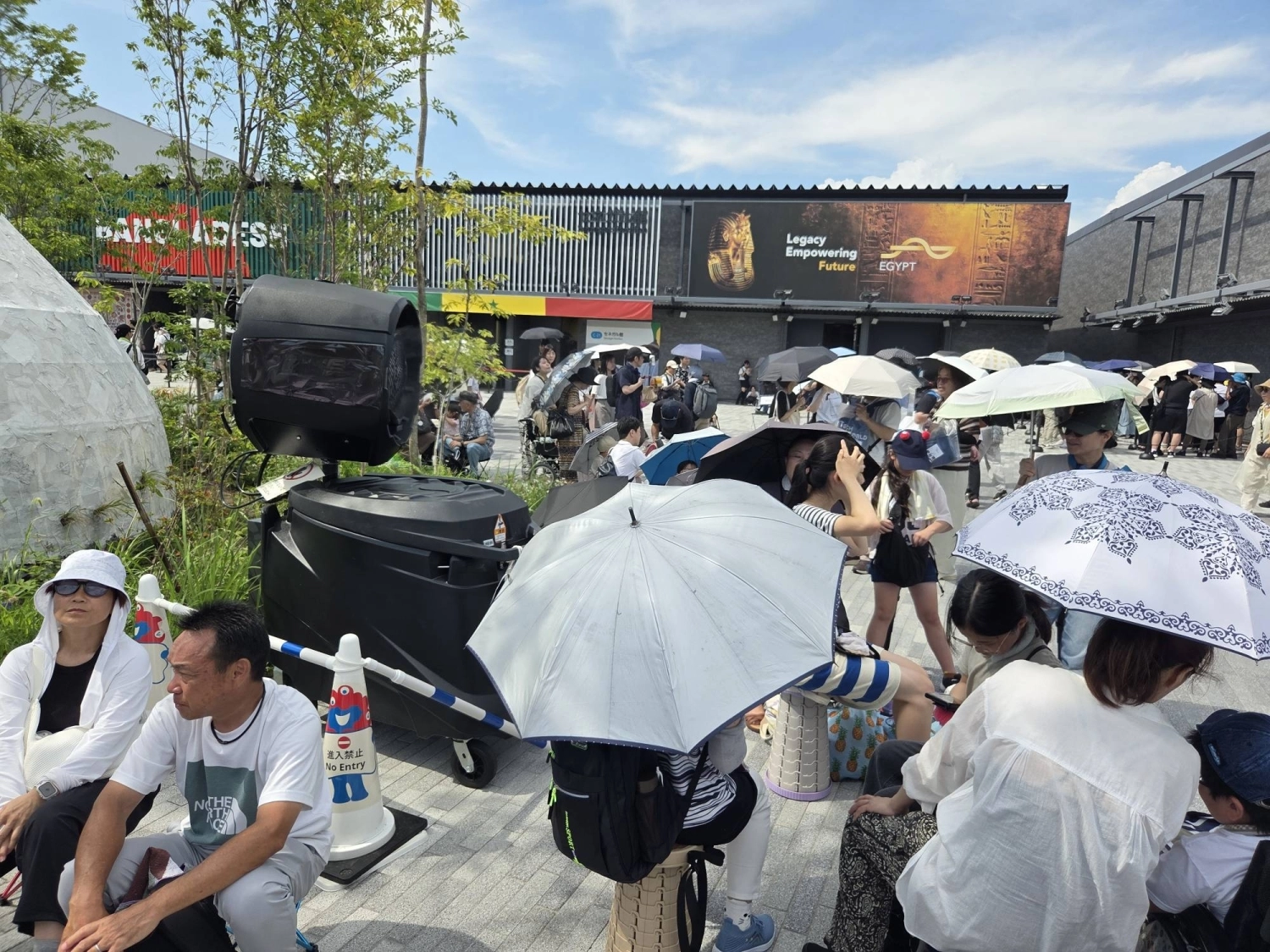 Visitors at the Osaka Expo in July sit near a large fan blowing mist. Visitors at the Osaka Expo in July sit near a large fan blowing mist.
