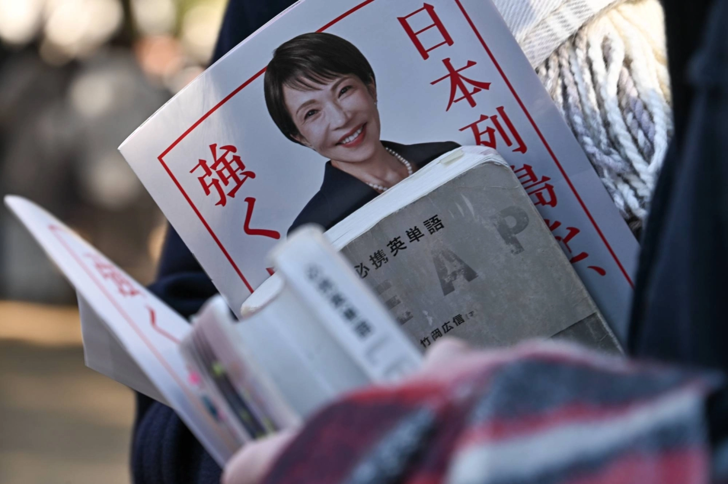週二,在埼玉市舉行的自民黨競選集會上,一名支持者手持自民黨總裁兼首相高市早苗的傳單,旁邊還有一本英語詞彙書。