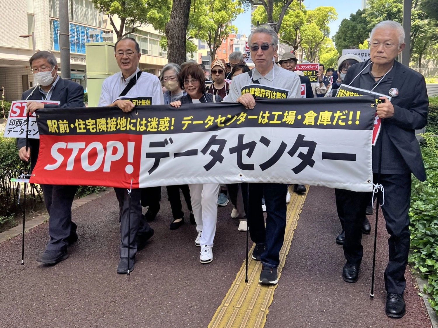Plaintiffs and supporters of a civil suit seeking to nullify a building permit for a planned data center in Inzai march toward the Chiba District Court on May 19 for the first hearing of the case. Plaintiffs and supporters of a civil suit seeking to nullify a building permit for a planned data center in Inzai march toward the Chiba District Court on May 19 for the first hearing of the case.