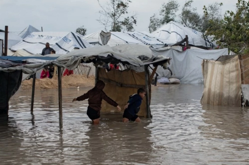 أطفال فلسطينيون نازحون يشقون طريقهم عبر شارع غمرته المياه عقب هطول أمطار غزيرة في خان يونس جنوب غزة.(إ ب أ)
